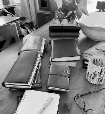 Leather notebooks, a pen and reading glasses on a wooden table